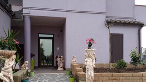 A building entrance with a stone pathway leading to a door, flanked by statues and planters.