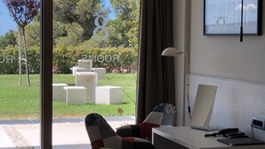 A modern hotel room with a bed, a desk with a laptop, and a view of a garden through a glass door. - Bel Etage Luxury Rooms (Split)