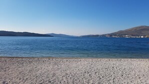 A beach with clear blue water, pebbly shore, and distant hills. - Bel Etage Luxury Rooms (Split)