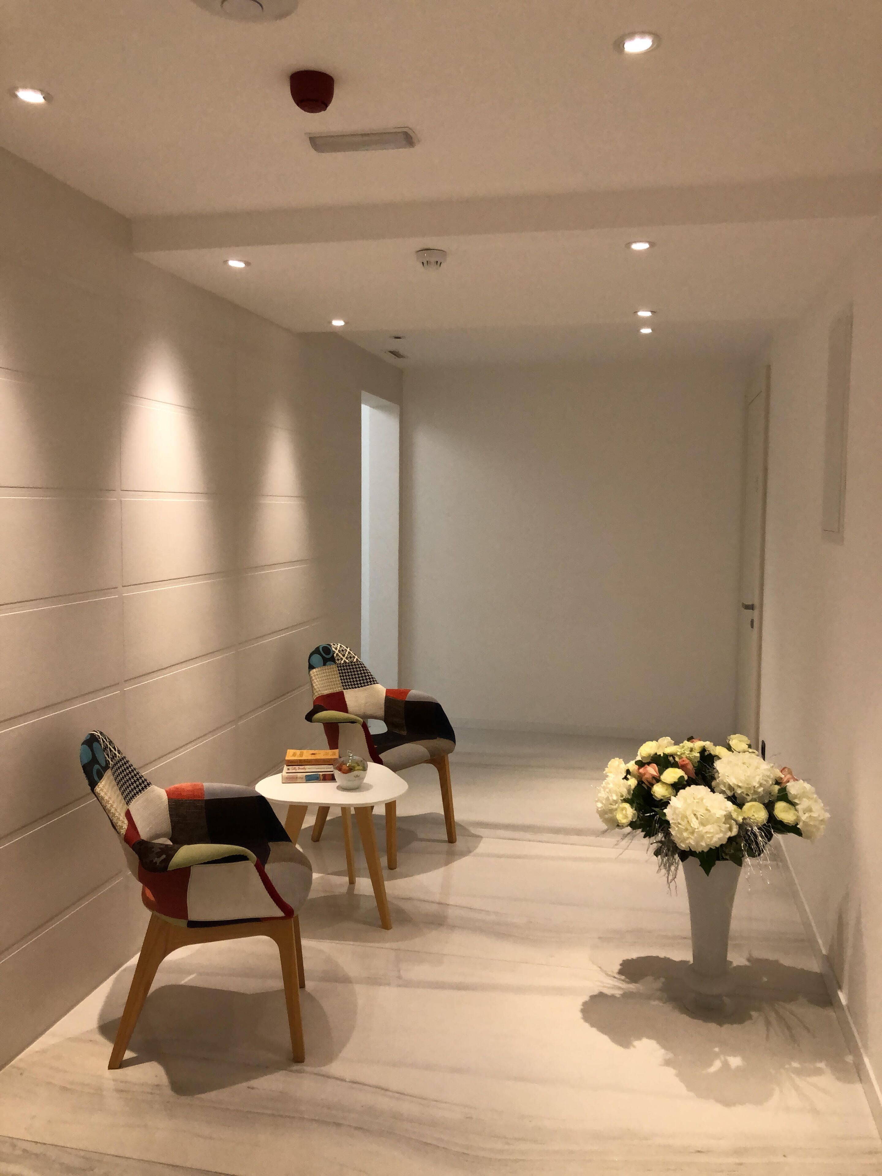 Een gang met twee stoelen, een tafel, een bloevas en inbouwspots.