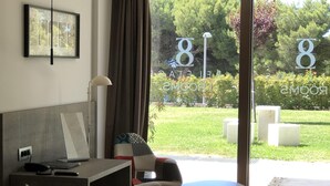 A hotel room with a bed, desk, chair, and a view of the garden through the glass door. - Bel Etage Luxury Rooms (Split)