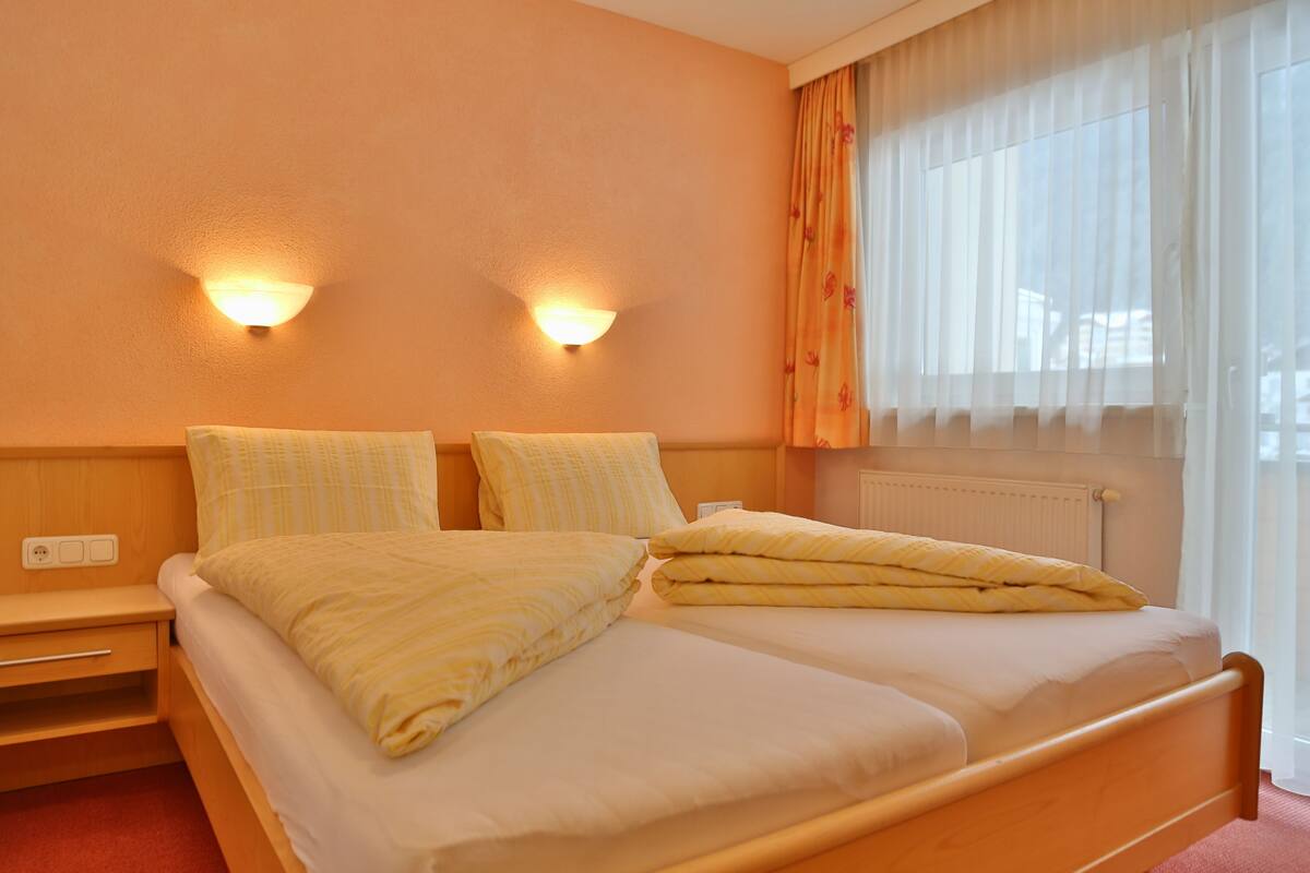 Una cama doble con cabecera de madera, dos mesitas de noche y dos lámparas fijadas a la pared.