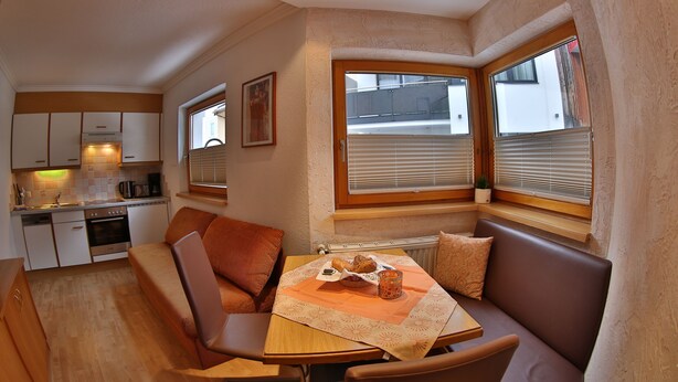 A compact kitchen with a dining area, including a table with a tablecloth, chairs, and a bench. - Apart Altamira (Ischgl)