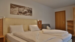 A hotel room with a large bed, a chair, a wooden door, and a wall-mounted picture. - Apart Altamira (Ischgl)