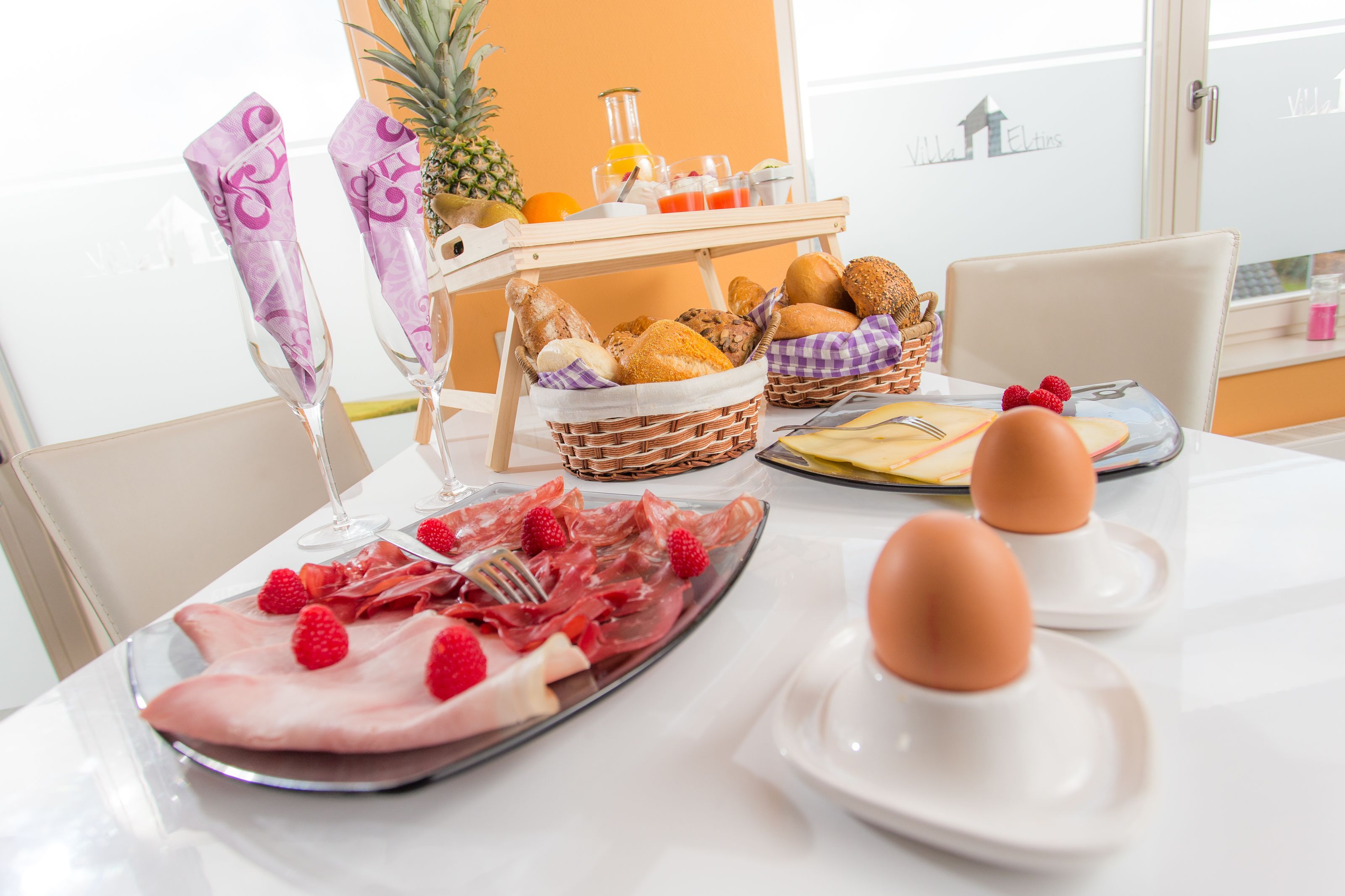 A breakfast setting with a variety of breads, pastries, and a fruit platter on a table.