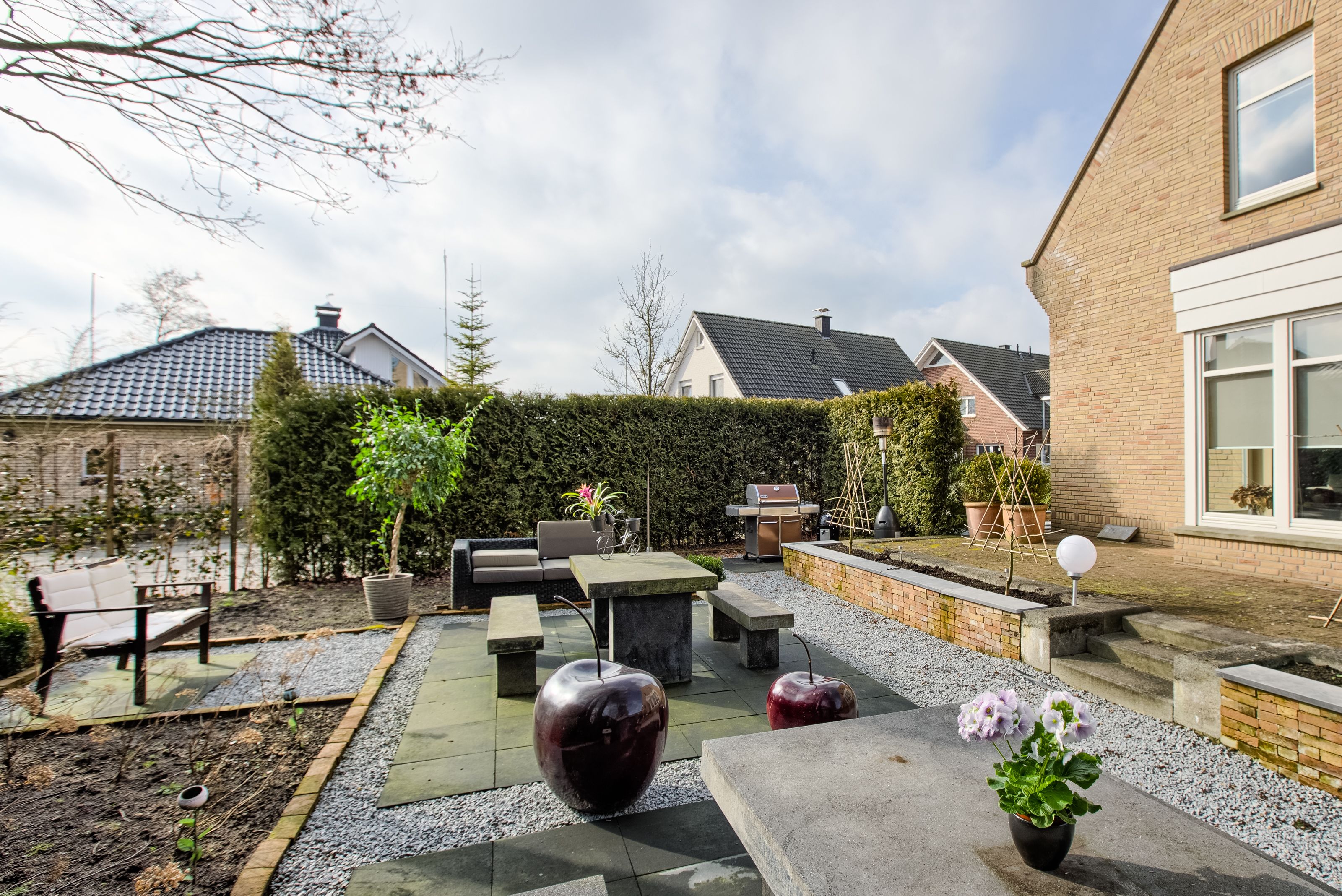 A patio area with outdoor furniture, a barbecue grill, and a garden with potted plants.