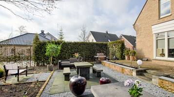 A patio area with outdoor furniture, a barbecue grill, and a garden with potted plants.