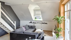 A modern loft apartment with a staircase, a sectional sofa, a dining table with purple placemats, and a large window. - Villa Eltins (Bad Bentheim)