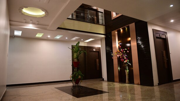 Un hall d’hôtel moderne avec un plafond haut, un balcon au deuxième étage et un espace d’accueil agrémenté d’un grand vase rempli de fleurs.