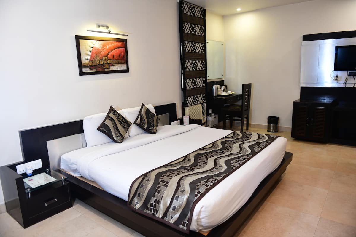 A modern hotel room with a large bed, a desk, a chair, and a television.