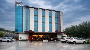 Un hôtel moderne, reconnaissable à son enseigne bien visible, qui s’étend sur plusieurs étages et dispose d’un parking où sont stationnées plusieurs voitures.