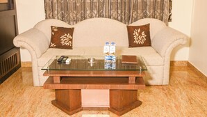 Un salon avec un canapé, deux coussins décoratifs, une table basse en verre et une télécommande.