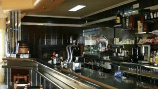 Un área de bar moderna con una barra alargada, taburetes y una variedad de botellas y vasos.