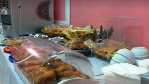 A buffet table with various food items covered in plastic containers and a cake on a red stand. - Hotel Michelangelo (Teramo)