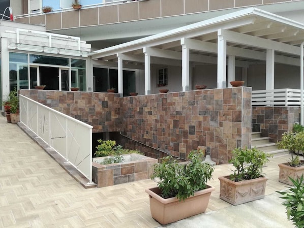 A covered outdoor area with a stone wall, potted plants, and a white railing.