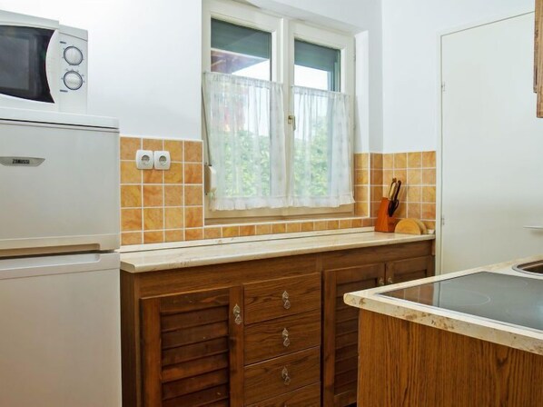 A kitchen with a microwave, a window with curtains, a tiled backsplash, wooden cabinets, and a countertop. - Apartment Vilma by Interhome (Balatonmariafurdo)