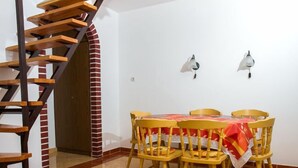 A dining area with a table set for four, surrounded by wooden chairs. A spiral staircase is visible to the left. - Apartment Vilma by Interhome (Balatonmariafurdo)