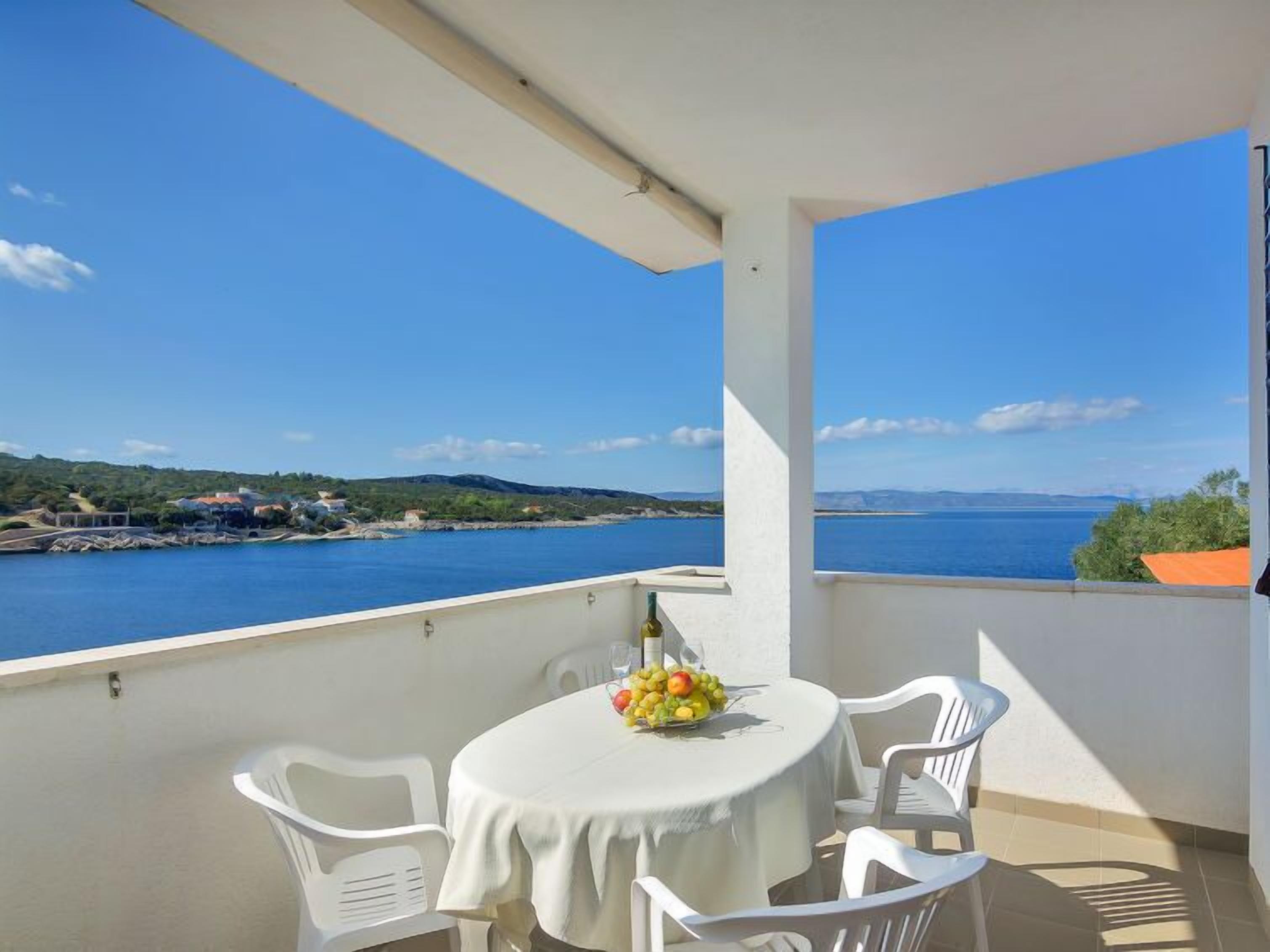 A balcony with a table set for two, overlooking a body of water and a distant coastline.