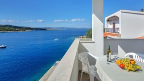 Un balcon avec une table dressée pour un repas, donnant sur une mer bleue et limpide où naviguent des bateaux.