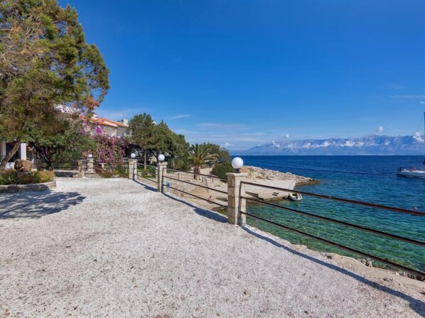 A coastal walkway with clear sea views, a rocky shoreline, and a mountainous backdrop.
