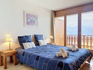 Een slaapkamer met een groot bed, twee nachtkastjes, een schilderij aan de muur en een balkon met uitzicht.