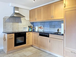 A modern kitchen with light wood cabinets, a black countertop, a stainless steel range hood, and a dishwasher.