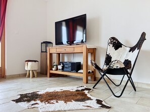 A living room with a flat-screen TV on a wooden stand, a leather chair, a small side table, and a cowhide rug. - Grand Panorama C5 by Interhome (Nendaz)