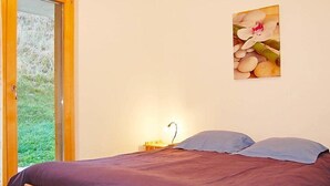 A bedroom with a bed, a nightstand, a lamp, and a window with a view of greenery. - Grand Panorama C5 by Interhome (Nendaz)