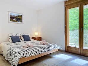 Une chambre à coucher avec un lit, des oreillers, une table de chevet avec une lampe, un tableau encadré au mur et une porte-fenêtre coulissante donnant sur un espace extérieur.