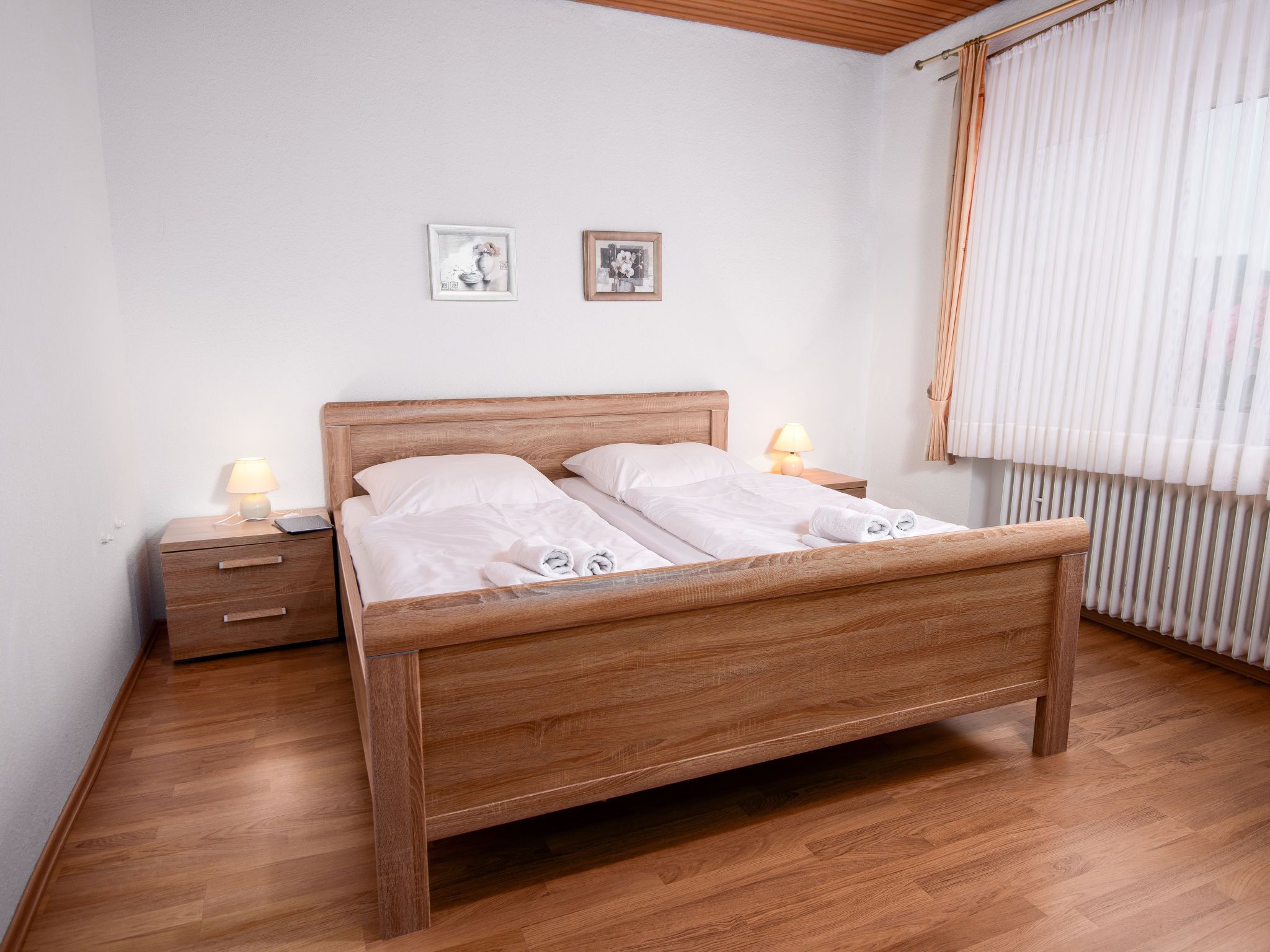 A neatly made bed with white linens, two bedside tables with lamps, and two framed pictures on the wall.