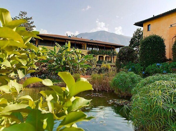 A building with a traditional architectural style, surrounded by lush greenery and a small pond. - Giardino by Interhome (Ascona)