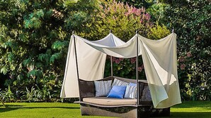 Ein Gartenambiente mit einer Korbschaukel und Baldachin, umgeben von üppigem Grün und blühenden Pflanzen.