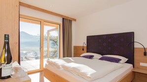 A modern bedroom with a large bed, wooden headboard, and a view of a mountainous landscape through a sliding glass door. - Kitzsteinhorn by Interhome (Zell am See)