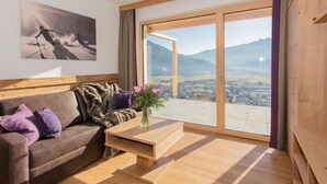 A modern living room with a sofa, a coffee table, and a large window offering a mountain view. - Kitzsteinhorn by Interhome (Zell am See)