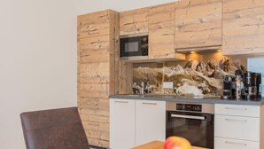 A modern kitchen with wooden cabinetry, a microwave, a coffee maker, and a bowl of apples on the counter. - Kitzsteinhorn by Interhome (Zell am See)