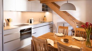 Eine moderne Küche mit weißen Schränken, einem Holzespeisetisch, der für zwei Personen gedeckt ist, und einer Treppe mit Holzgeländer.