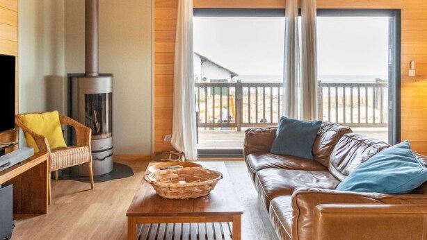 A cozy room with a fireplace, a sofa, a wicker basket, and a wooden table. - Les Mouettes by Interhome (Mimizan)