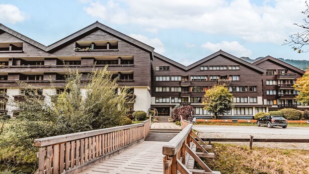 A modern multi-story building with balconies, a wooden bridge, and a parking area. - Apartment Römer by Interhome (Bad Hofgastein)