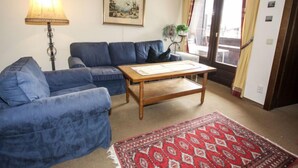 A living room with a blue sofa, a wooden coffee table, a lamp, a painting, and a red patterned rug. - Apartment Römer by Interhome (Bad Hofgastein)