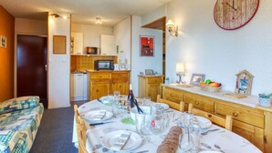 Un comedor acogedor con una mesa dispuesta para cuatro, un microondas en la cocina y un reloj en la pared.
