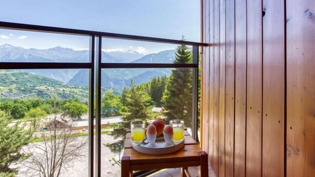 Ventana de madera con una bandeja de desayuno sobre una mesa, con vistas a un paisaje montañoso.