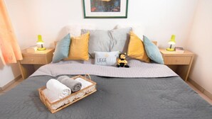 Ein ordentlich eingerichtetes Hotelzimmer mit einem großen Bett, zwei Nachttischen mit Lampen, einem gerahmten Bild an der Wand und einem W äschekorb mit Handtüchern auf dem Bett.