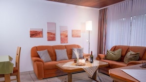 Ein gemütliches Wohnzimmer mit zwei orangenen Sofas, einem Holztisch und einer Stehlampe.