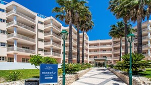 L’entrée d’un hôtel, avec un panneau indiquant la réception, des palmiers et un chemin pavé menant au bâtiment.