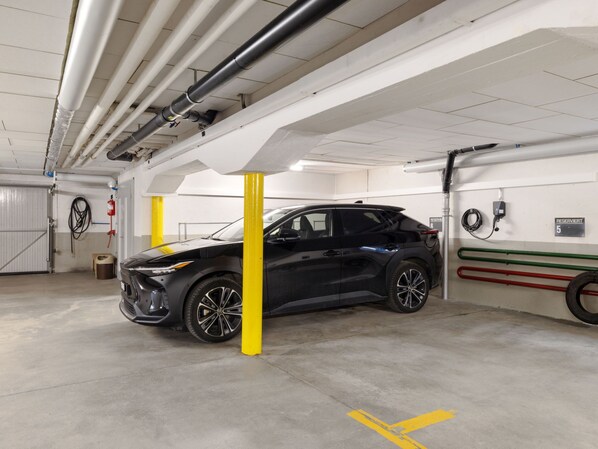 Autotalli, jossa on musta maasturi pysäköitynä sille varattuun paikkaan. Seinät ovat valkoiset ja katossa on näkyvissä putkia.