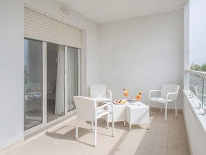 Un balcon agrémenté de meubles en osier blanc, une porte vitrée et une petite table sur laquelle sont disposés des fruits et une boisson.