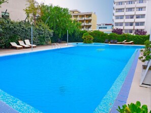 Une piscine avec des chaises longues et un petit palmier.