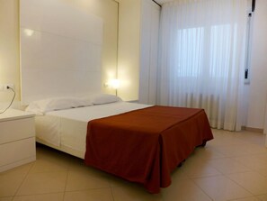 Une chambre d’hôtel avec un lit, une table de chevet, une lampe et une fenêtre avec des rideaux.
