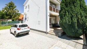Ein zweistöckiges Haus mit weißer Fassade, ein Auto auf der Auffahrt und ein großer, grüner Baum im Vorgarten.