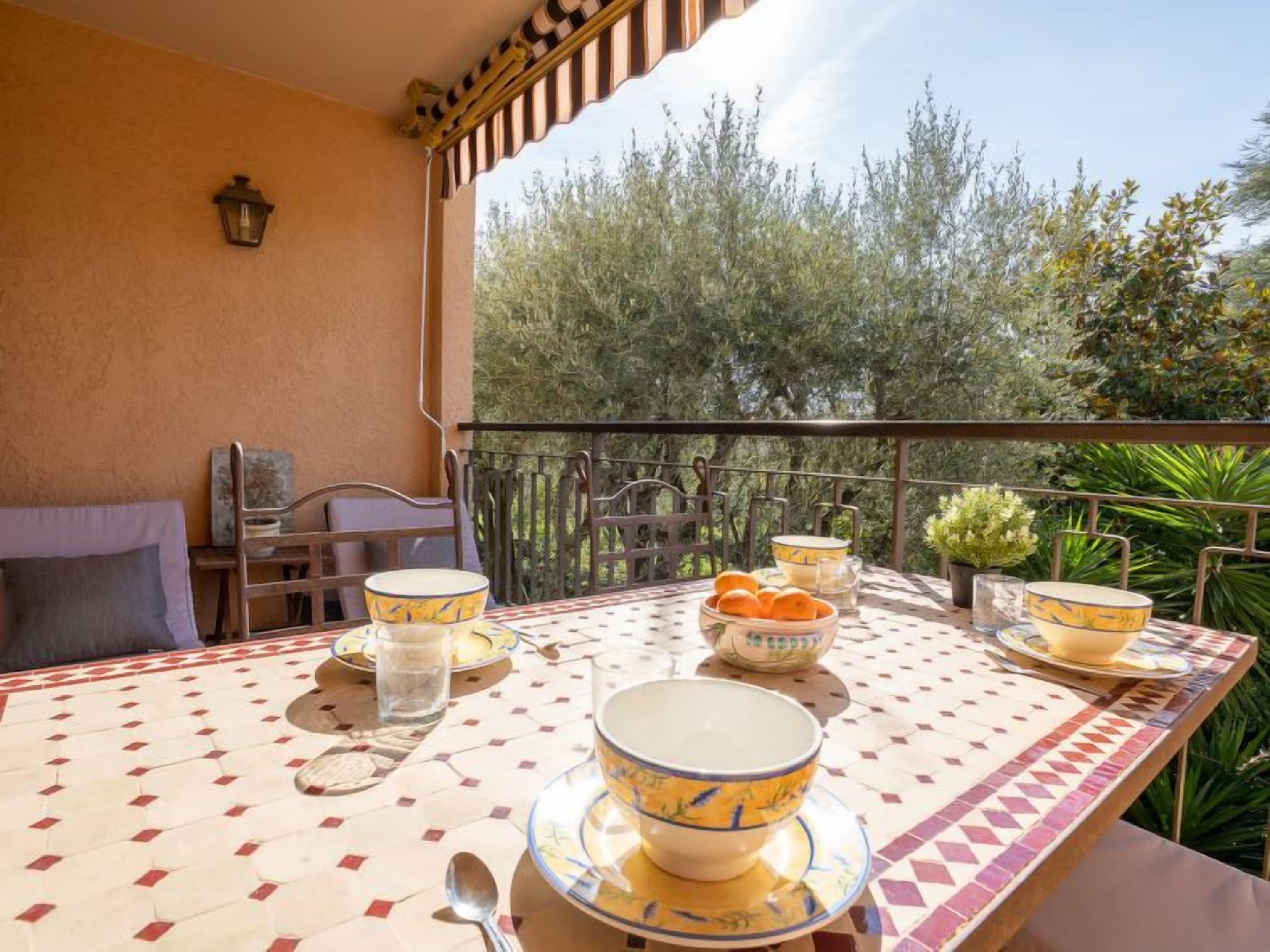 A dining table set with bowls and glasses, a chair, a small table with a lamp, and a view of trees and plants.